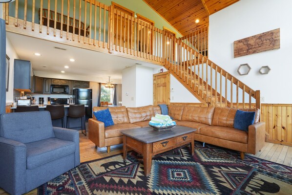 A spacious living area with a high wooden staircase, a leather sofa, a blue armchair, and a wooden coffee table.