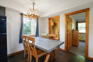 A modern kitchen with a dining table, chairs, a chandelier, and a refrigerator.