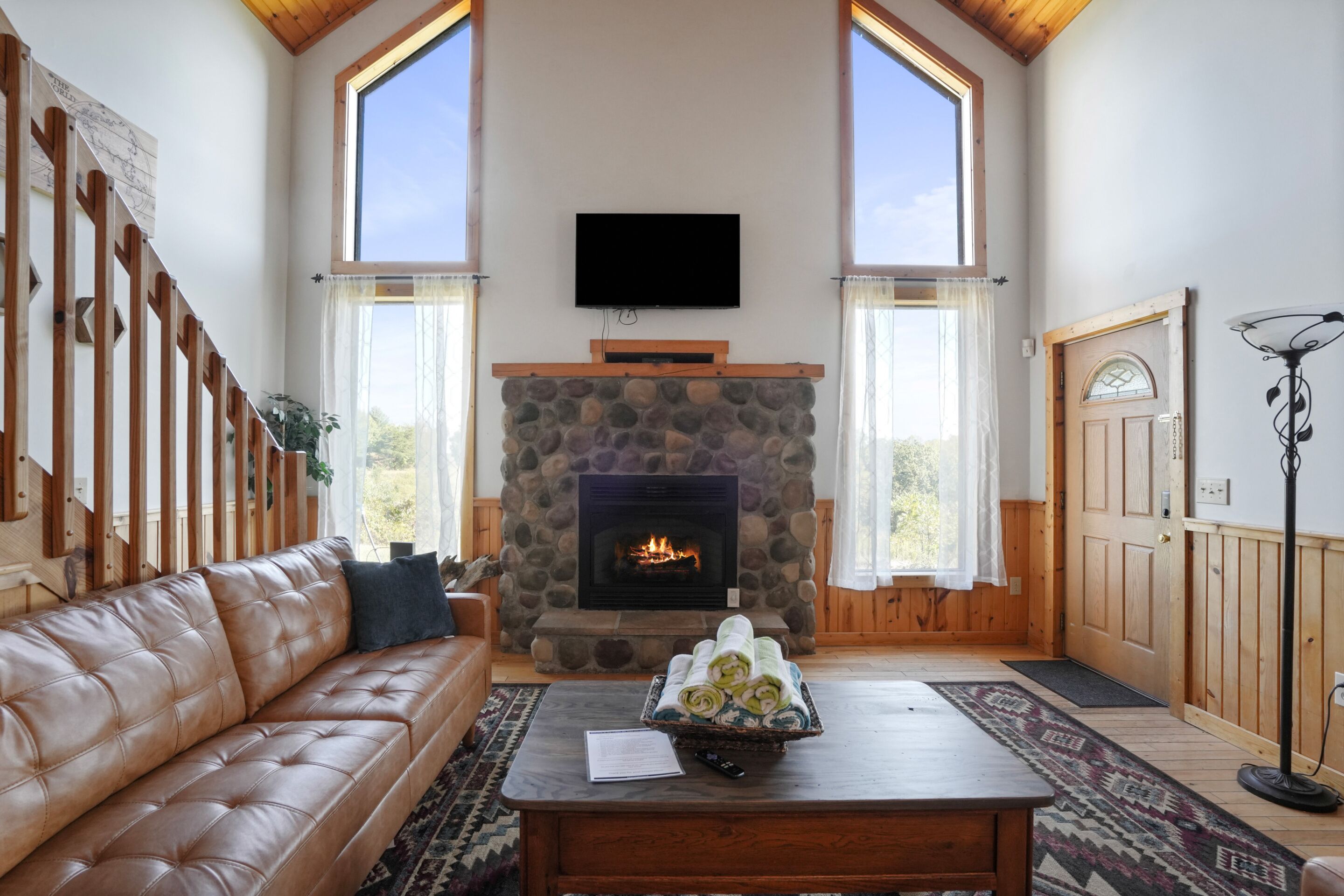 A cozy living room with a stone fireplace, a leather sofa, a coffee table, and a TV mounted on the wall.