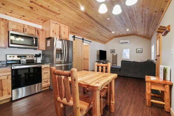 A modern kitchen with wooden cabinets, stainless steel appliances, and a dining area with a wooden table and chairs. - Ridge Point Cabin | Hocking Hills, Secluded (Rockbridge)