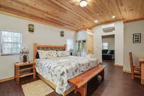 A bedroom with a wooden ceiling, a bed with a deer-patterned blanket, a wooden bench, and a small table with a lamp. - Ridge Point Cabin | Hocking Hills, Secluded (Rockbridge)