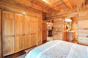 Interno di una baita in legno con un letto grande, un armadio in legno e un bagno con lavandino e specchio.