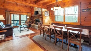 Ein gemütliches Blockhäuschen-Interieur mit Kamin aus Stein, einem Holzespeisetisch und bequemen Sitzgelegenheiten.