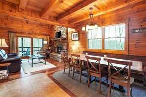 A cozy cabin interior with a stone fireplace, wooden dining table, and comfortable seating.