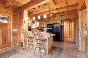 Ein Holzblockhaus-Innenraum mit Küchenbereich, der eine zentrale Kochinsel mit Barhocker, einem Kühlschrank und einem Herd beinhaltet.