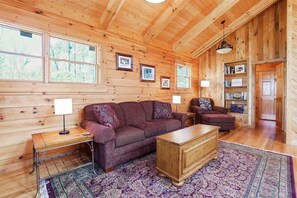 L'interno accogliente di una baita di legno, con un divano grande, una poltrona più piccola, un tavolino in legno e un tappeto decorato.