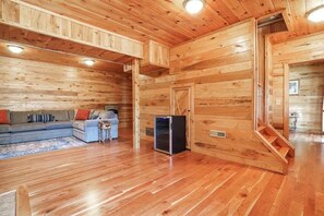 A log cabin interior with a wooden floor, a sofa, a small table, and a refrigerator. - Hidden Haven | Hocking Hills, Sleeps 8, Hot Tub (Laurelville)