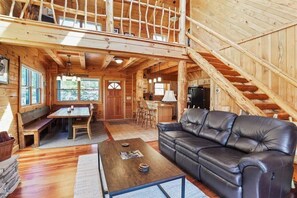 Eine geräumige Holzhütte mit Essbereich, einer Couch und einer Treppe.
