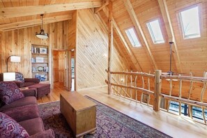 Un intérieur en bois avec une mezzanine, un canapé, une bibliothèque et un escalier.