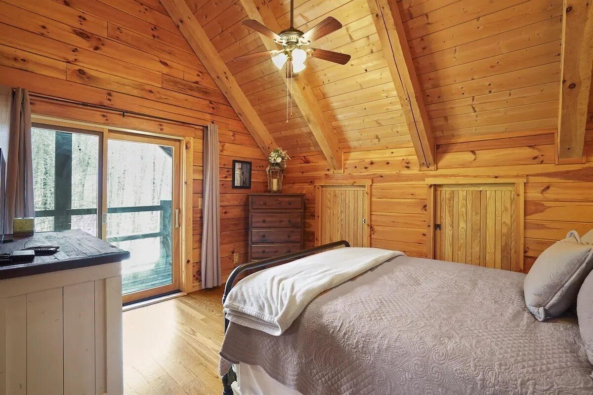 A wooden cabin bedroom with a bed, dresser, and a ceiling fan.