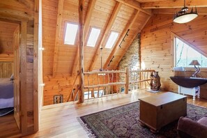 A wooden interior with a sloped ceiling, a staircase, a bear statue, a table, and a window. - Hidden Haven | Hocking Hills, Sleeps 8, Hot Tub (Laurelville)