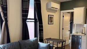 Ett modernt vardagsrum med en grå soffa, en mönstrad matta och en matplats med ett litet bord och stolar.
