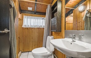 Ein Badezimmer einer Holzhütte mit Toilette, Waschbecken und Duschvorhang.