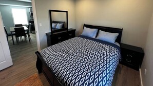 A bedroom with a bed, bedside tables, a dresser, a mirror, and a dining area with chairs and a table. - Almira Properties Unit 3 (Providence)