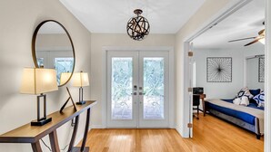 Un interior moderno con piso de madera, un escritorio con lámparas, un espejo grande, una lámpara decorativa en el techo y vistas a través de puertas con vidrio esmerilado.