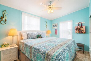 Quarto com cama, duas mesas de cabeceira, ventilador de teto e janela com persianas.