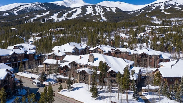 A snow-covered lodge with multiple buildings, surrounded by trees and mountains.