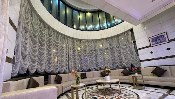 Un hall d’entrée luxueux, doté d’un espace salon aux lignes courbes, d’un sol en marbre et d’une grande fenêtre agrémentée de rideaux.