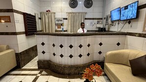 Un espace d’accueil d’hôtel avec un comptoir incurvé, un bureau de réception, deux téléviseurs fixés au mur, un canapé, une table basse et un vase rempli de fleurs.