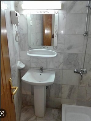 Une salle de bain avec un lavabo sur colonne, un miroir et une douche.