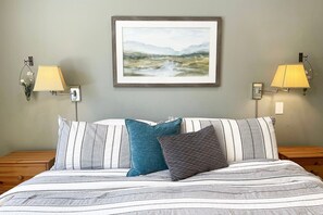 Ein Bett mit gestreifter Bettwäsche, zwei Wandlampen und ein gerahmtes Landschaftsbild darüber.