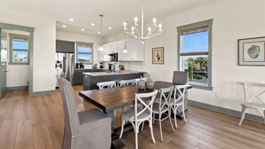A modern kitchen with white cabinets, stainless steel appliances, and a wooden dining table with white chairs.