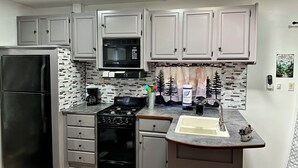 A kitchen with grey cabinets, a black refrigerator, a microwave, a stove, and a sink. - Mountain Dreams, up to date camper with WiFi & fireplace (Cosby)