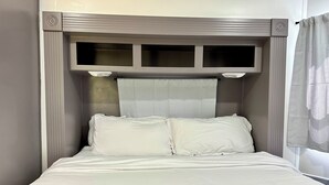A bed with a headboard, white bedding, and a window with curtains. - Mountain Dreams, up to date camper with WiFi & fireplace (Cosby)