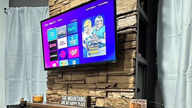 A flat-screen TV mounted on a stone wall above a fireplace with a sign that reads "THE MOUNTAINS ARE MY HAPPY PLACE." - Mountain Dreams, up to date camper with WiFi & fireplace (Cosby)