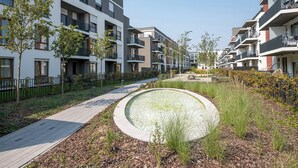 Un edificio residencial moderno con balcones, un camino pavimentado y una fuente circular.