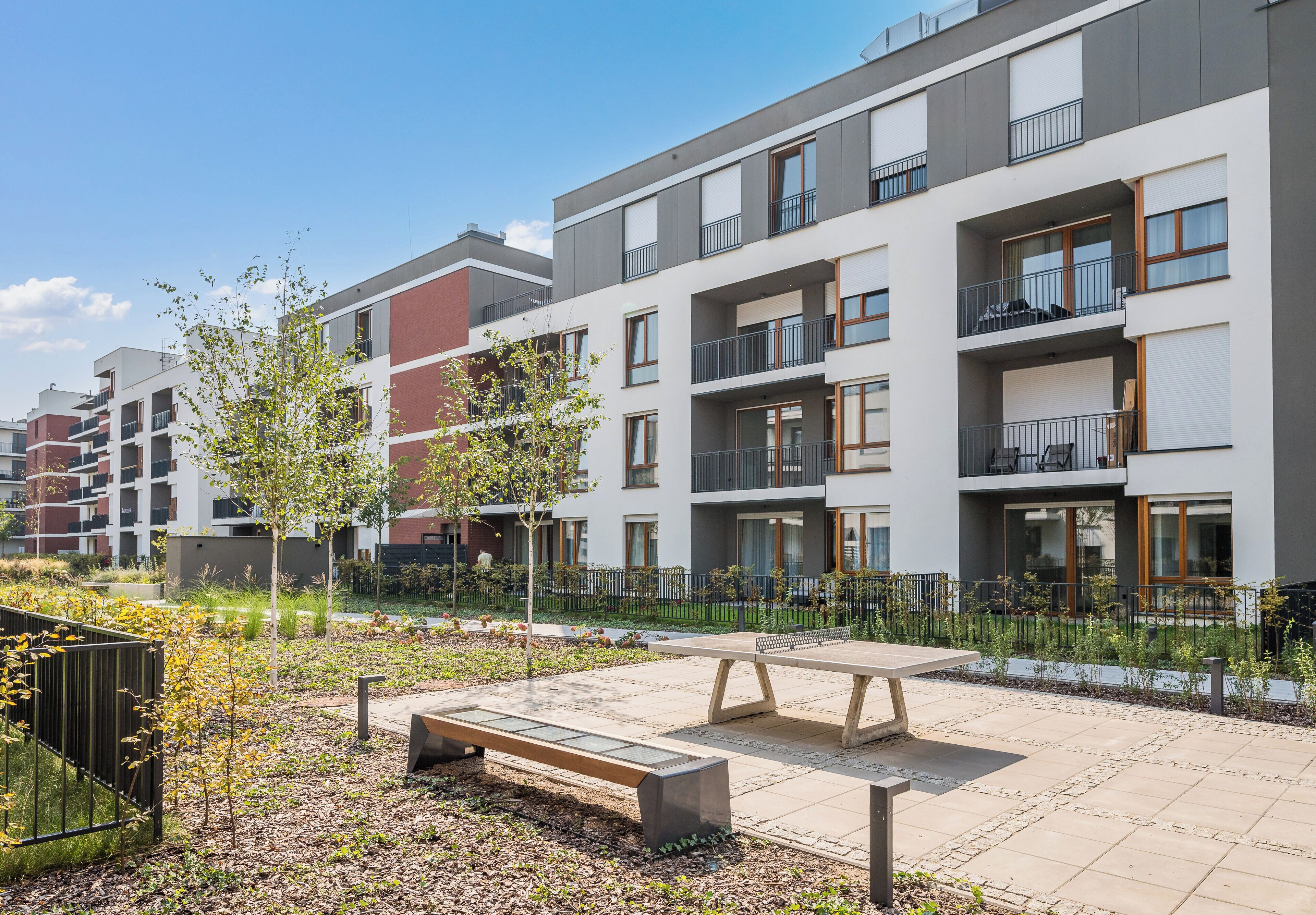 Un immeuble d’appartements moderne doté de balcons, d’une cour avec un banc et d’un petit jardin.