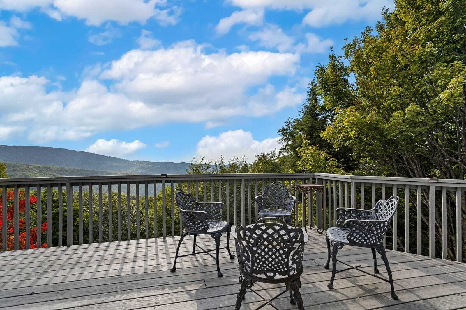 A deck with a view of mountains, three wicker chairs, and a table.