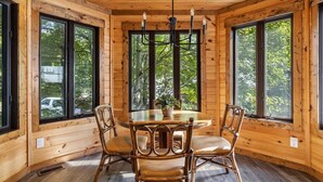 A wooden cabin interior with a round dining table, four chairs, and a chandelier.