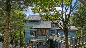 A two-story house with a wooden staircase leading to a balcony, surrounded by trees.