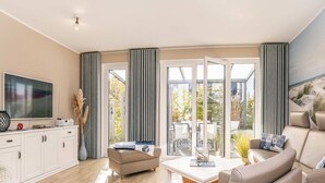 A modern living room with a sofa, a coffee table, a TV, and a dining area with chairs and a table. - Vacation home Usedom-Idyll - Modern vacation home with beach chair - only 700 m to the beach (Loddin)