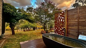 Un jardín con una terraza de madera, una fuente de agua negra grande y una valla decorativa de metal.
