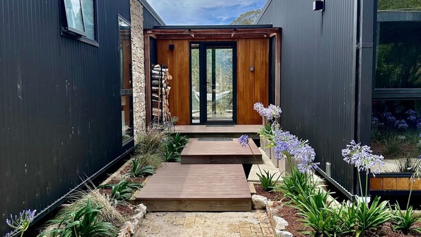 Een modern huis met een houten terras dat leidt naar een glazen voordeur.