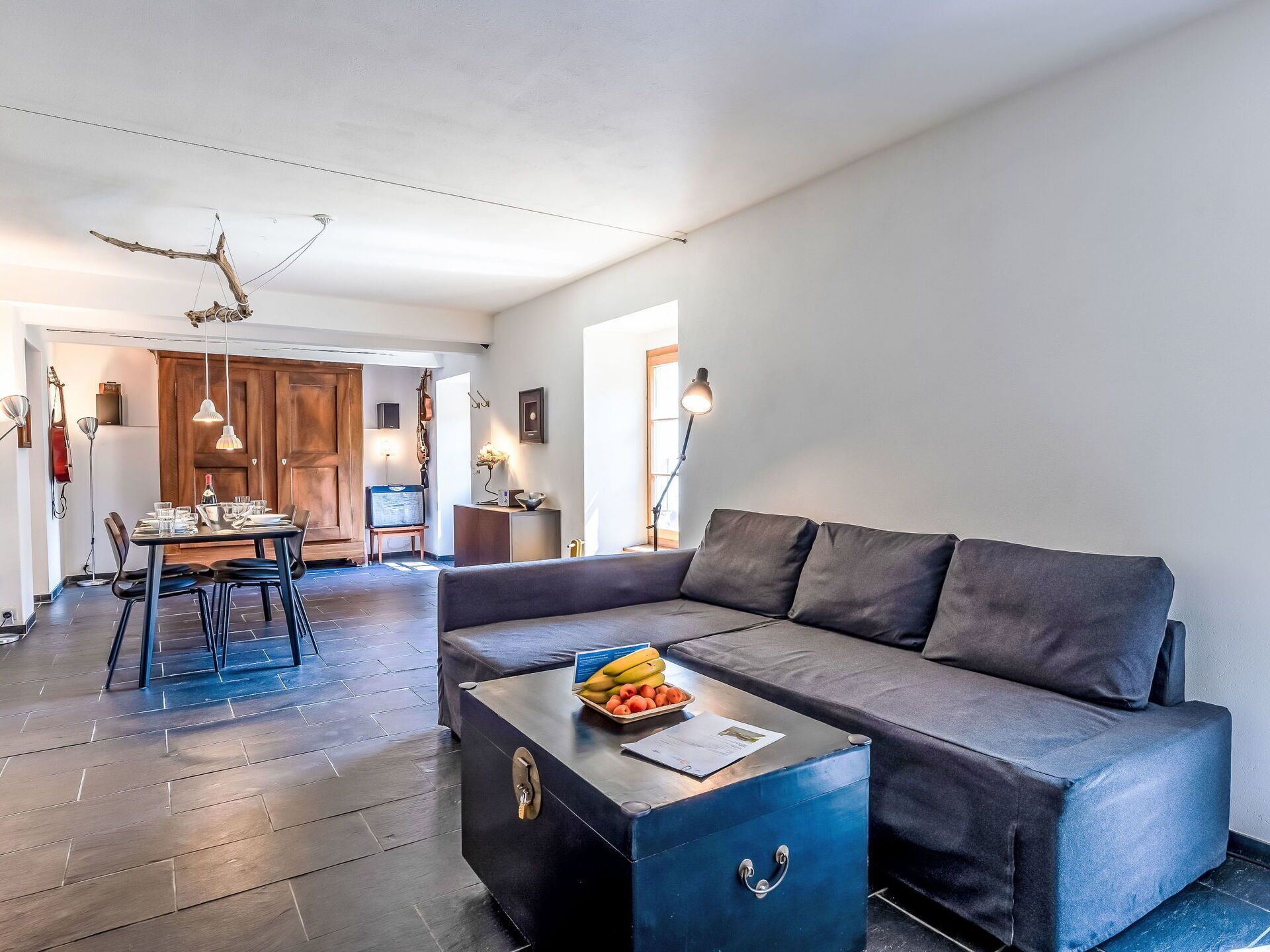 Un salon moderne avec un canapé, une table basse sur laquelle sont disposés des fruits, et un coin repas comprenant des chaises et une table.