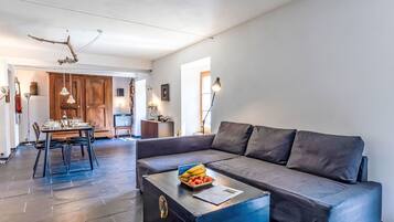 Un salon moderne avec un canapé, une table basse sur laquelle sont disposés des fruits, et un coin repas comprenant des chaises et une table.