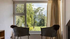 Ein Zimmer mit zwei Sesseln vor einem Fenster mit Blick auf eine grüne Landschaft.