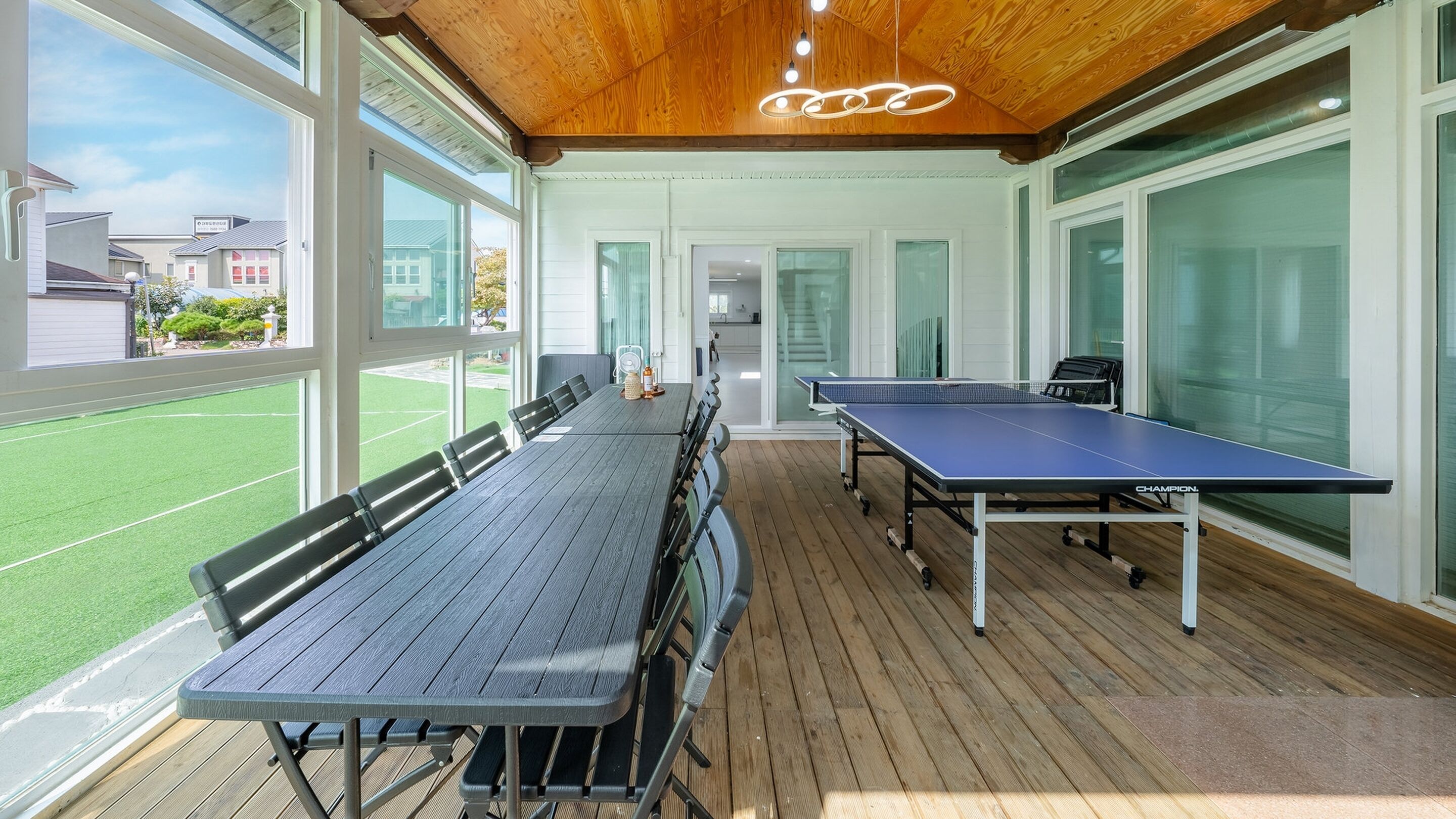 A covered outdoor area with a ping pong table and seating, large windows, and a wooden ceiling.
