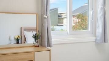Een slaapkamer met een houten dressoir, een spiegel, een vaas met bloemen en een raam met gordijnen.