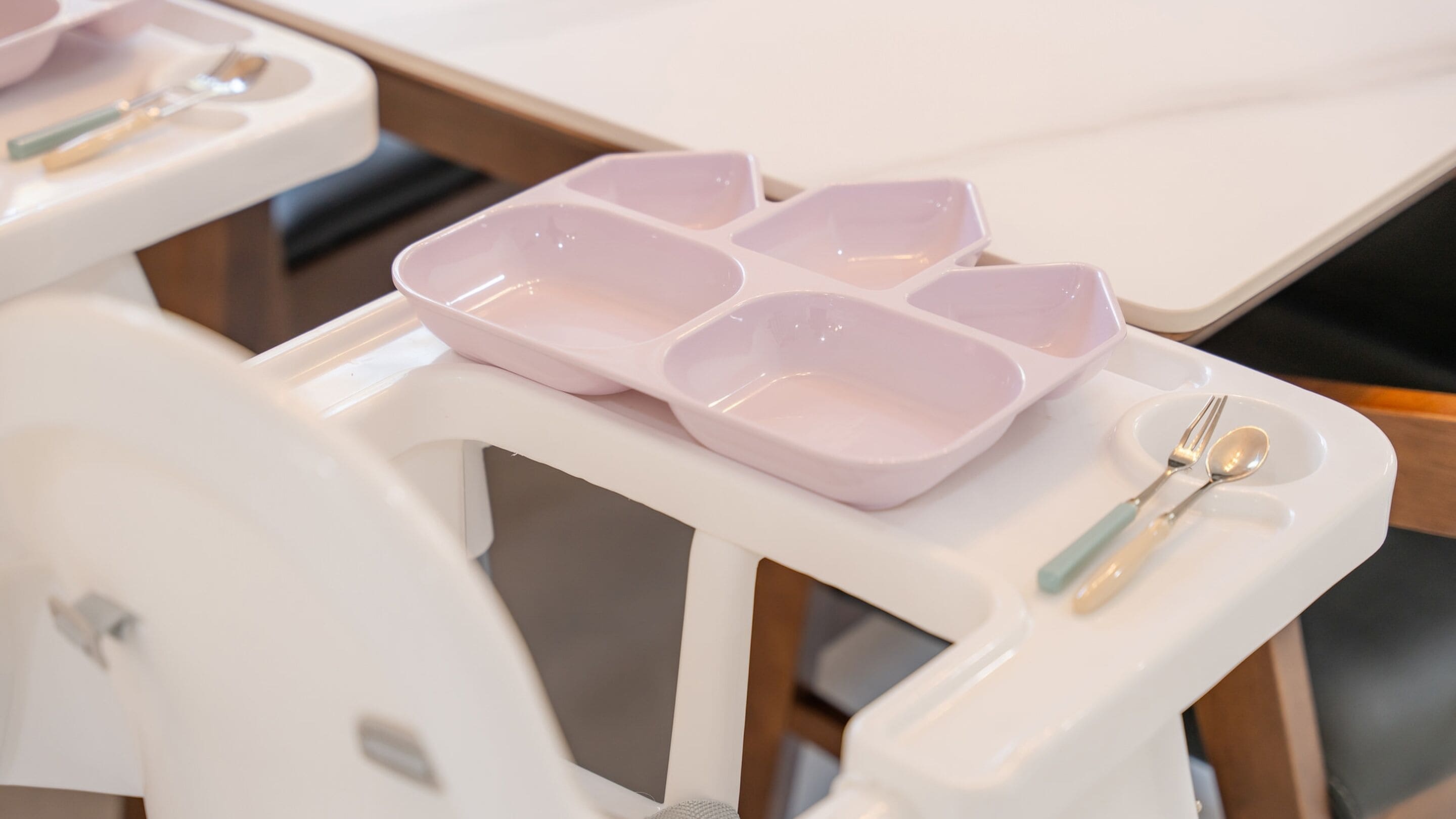 A white tray table with a pink tray and utensils.