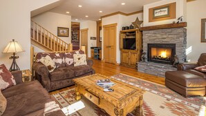 A spacious living room with a fireplace, leather sofas, a wooden coffee table, and a staircase leading to another level. - Private hot tub, multiple private decks, near Town Center - Spanish Peaks Perfection (Big Sky)