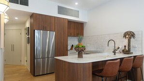Uma cozinha moderna com armários de madeira, geladeira de aço inoxidável, bancada branca e um espaço com banquetas.