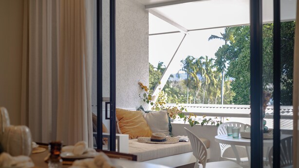 Quarto moderno com cama, mesa de jantar e vista para palmeiras.