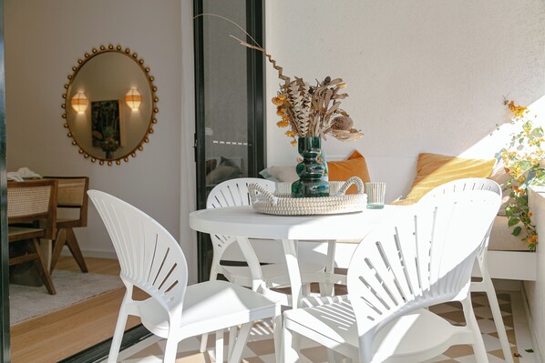 A white dining table with chairs, a vase with dried flowers, and a mirror with lights on the wall. - Monsoon Luxury Apartment in the heart of Macrossan Street (Port Douglas)