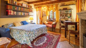 Une pièce chaleureuse avec un plafond en bois, un lit recouvert d’une literie à motifs floraux, une bibliothèque, un bureau et une chaise.
