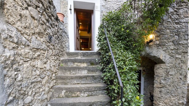 Un escalier en pierre menant à l’entrée d’un bâtiment, entouré de verdure et de murs en pierre.