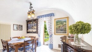Un coin repas avec une table et des chaises en bois, un lustre, une étagère avec des assiettes, un tableau et un vase décoré de plantes.